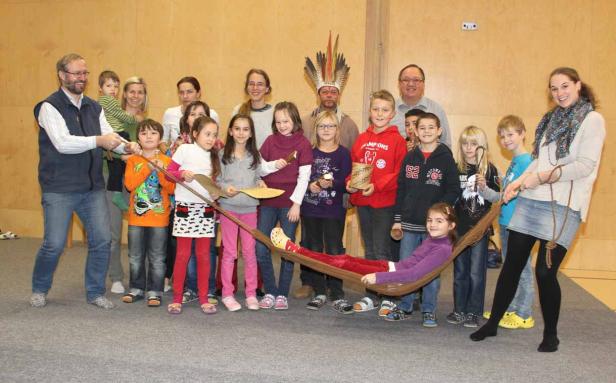 Eine Gruppe von Kindern und Erwachsenen spielt ein Spiel mit einer Hängematte und Holzpaddeln.