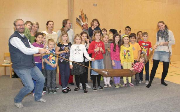 Eine Gruppe Kinder und Erwachsene zieht an einem hölzernen Spielboot.