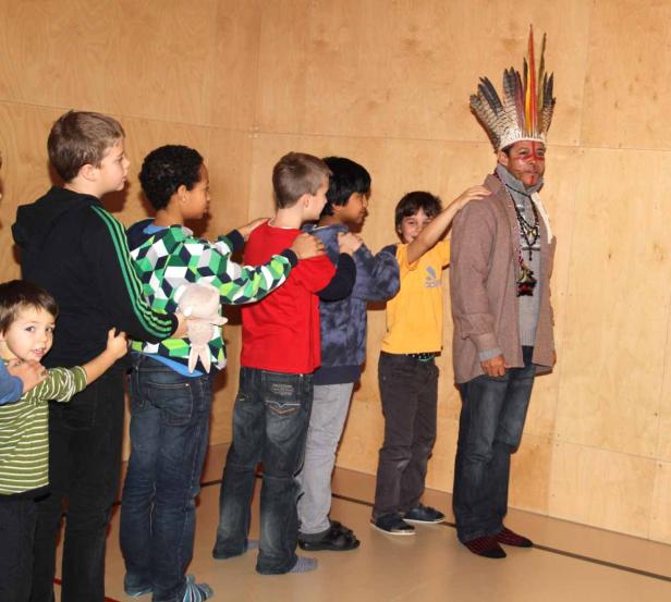 Eine Gruppe Kinder steht hinter einem Mann mit Kopfschmuck und bemaltem Gesicht.