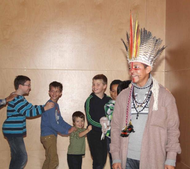 Ein Mann mit Kopfschmuck und Gesichtsbemalung steht vor einer Gruppe von Kindern.