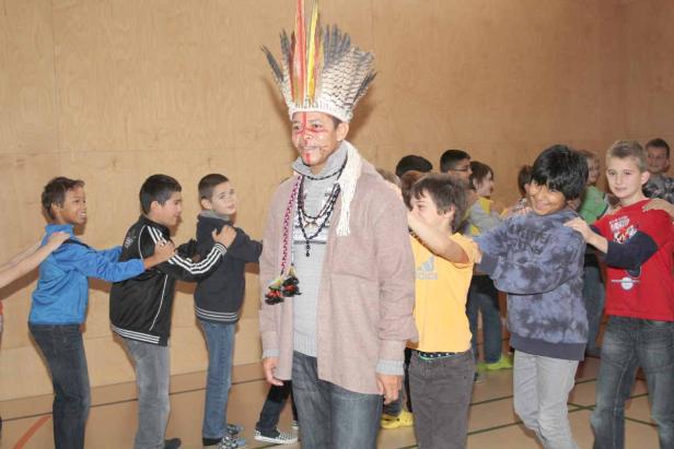 Ein Mann mit Federschmuck wird von einer Gruppe Kindern umringt.