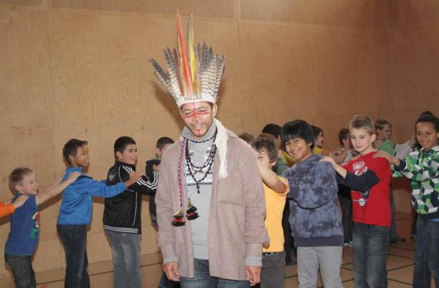 Ein Mann mit indianischem Kopfschmuck steht inmitten einer Gruppe von Kindern.