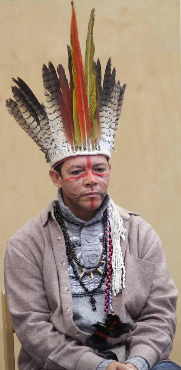 Ein Mann mit Gesichtsbemalung und Federschmuck blickt ernst.