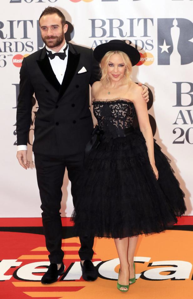 Kylie Minogue und ein Mann in Anzügen posieren auf dem roten Teppich.