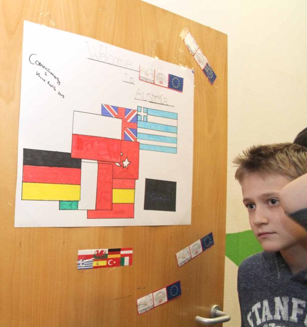 Ein Junge betrachtet ein Plakat mit Flaggen und der Aufschrift „Welcome to Austria“.
