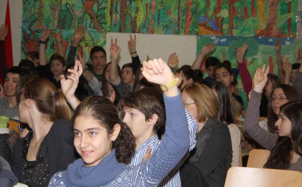 Eine Gruppe von Schülern sitzt in einem Raum und hebt die Hände.