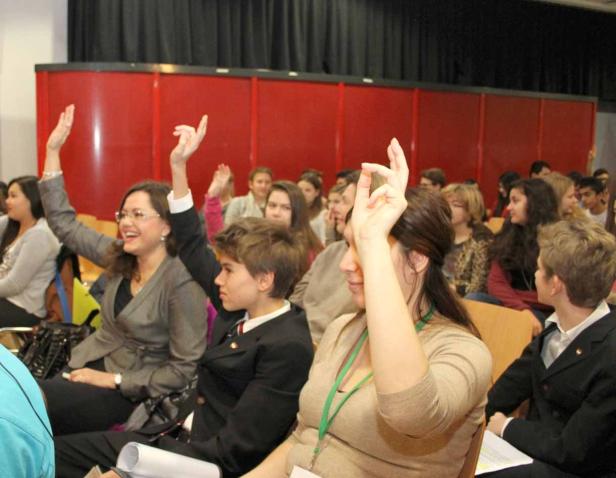 Eine Gruppe von Menschen sitzt in einem Raum und hebt die Hände.