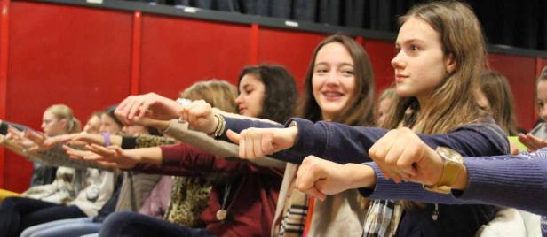 Eine Gruppe Jugendlicher sitzt und streckt die Arme nach vorne.