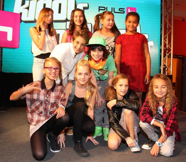 Eine Gruppe von neun Kindern posiert vor einer Leinwand mit dem Schriftzug „PULS 4“.