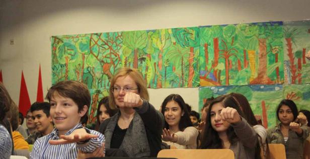 Eine Lehrerin und eine Gruppe von Schülern machen eine gemeinsame Geste vor einem Dschungelbild.
