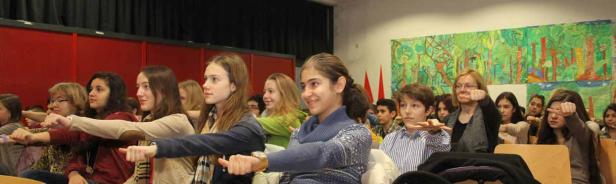 Eine Gruppe von Schülern und eine Lehrerin machen Dehnübungen im Klassenzimmer.