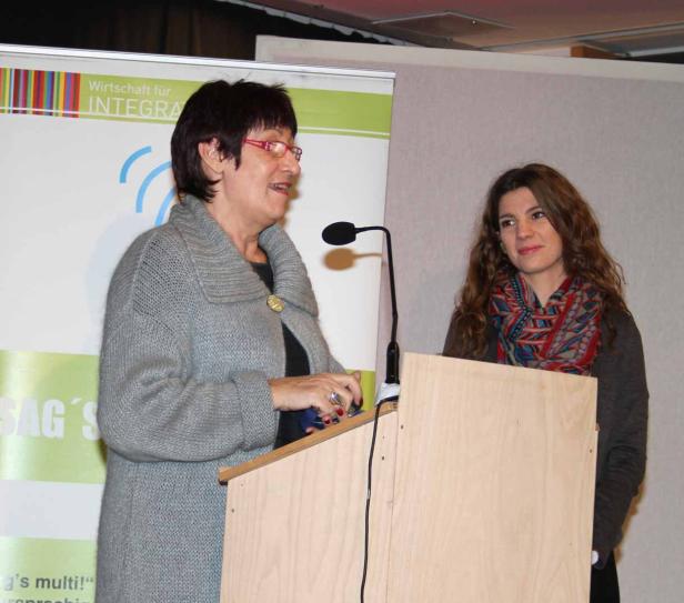 Eine Frau hält eine Rede an einem Rednerpult, während eine andere Frau daneben steht.