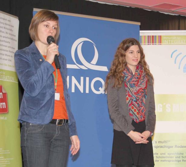 Zwei Frauen stehen vor einem Banner von „UNIQ“ und sprechen.