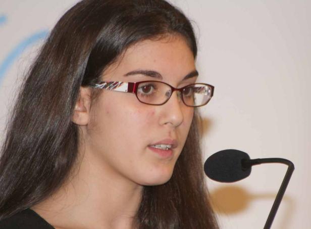 Eine junge Frau mit Brille spricht in ein Mikrofon.
