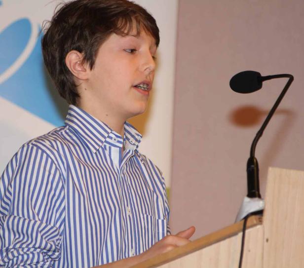 Ein junger Mann mit Zahnspange hält eine Rede an einem Rednerpult.