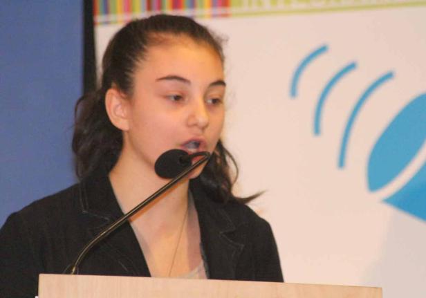 Eine junge Frau spricht bei einer Veranstaltung in ein Mikrofon.