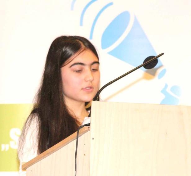 Eine junge Frau steht an einem Rednerpult und spricht.