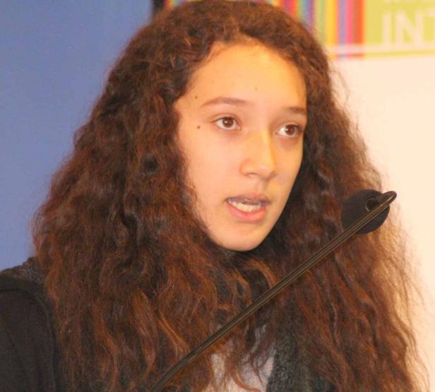 Eine junge Frau mit lockigem Haar spricht an einem Mikrofon.