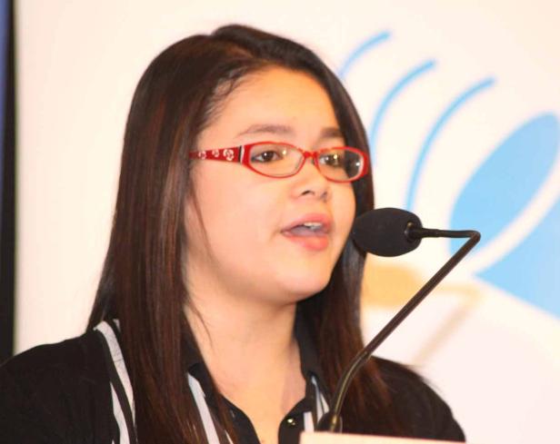 Eine junge Frau mit roter Brille spricht in ein Mikrofon.