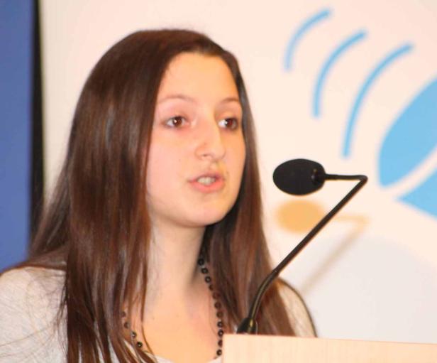 Eine junge Frau spricht an einem Rednerpult in ein Mikrofon.