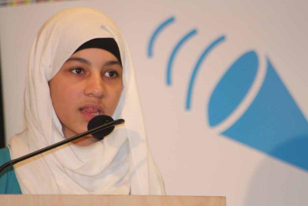Ein junges Mädchen mit Hijab spricht an einem Mikrofon.