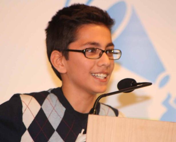 Ein junger Mann mit Brille lächelt an einem Rednerpult ins Publikum.