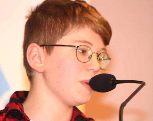 Ein junger Mann mit Brille spricht in ein Mikrofon.