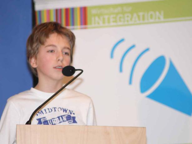 Ein junger Redner steht am Pult vor einem Integrations-Hintergrund.