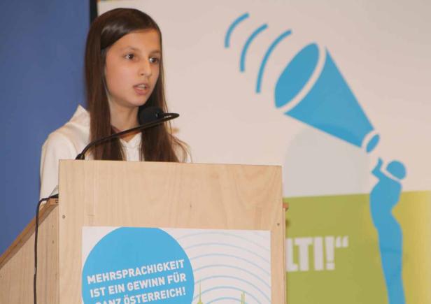 Ein junges Mädchen spricht an einem Rednerpult vor einem Publikum.