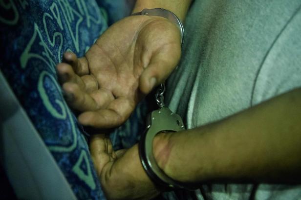 Ein Mann liegt mit Handschellen gefesselt auf einer gemusterten Oberfläche.