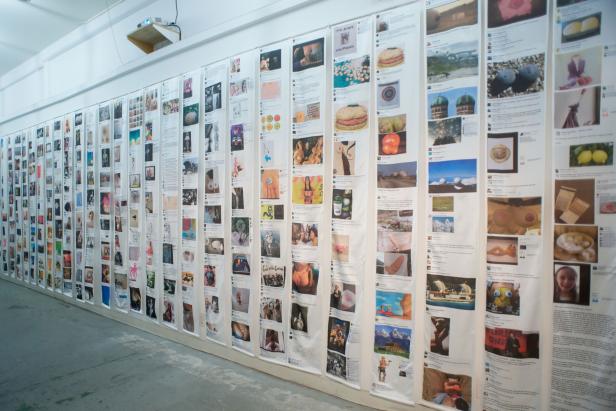 Eine Wand in einer Galerie ist mit vielen bedruckten Stoffbahnen behangen.