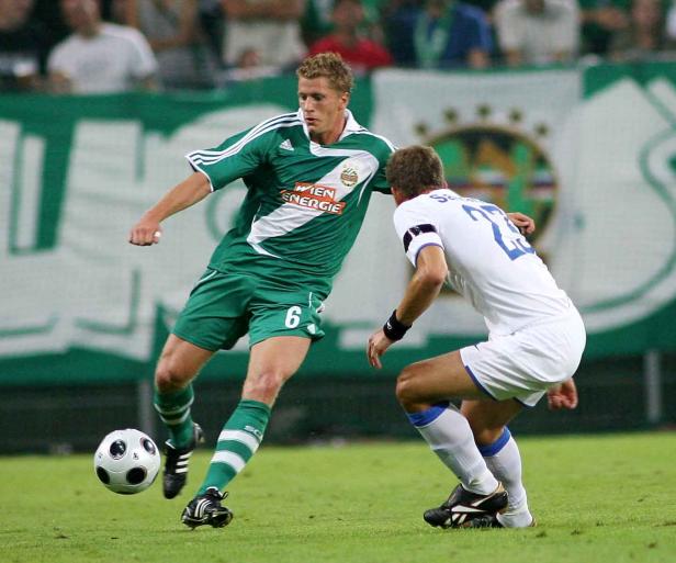 Ein Fußballspieler in Grün dribbelt den Ball, während ein Gegenspieler ihn zu stoppen versucht.