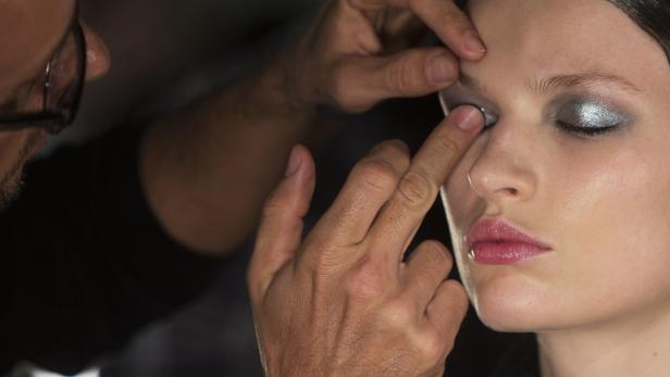 Ein Visagist trägt silbernen Lidschatten auf ein Model auf.