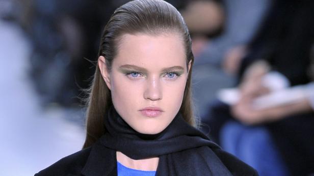 Porträt einer Frau mit zurückgekämmtem Haar und grünem Lidschatten.