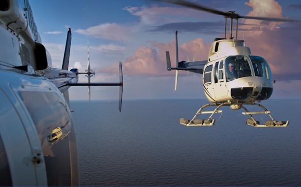 Zwei Hubschrauber fliegen über das Meer vor einem bewölkten Himmel.