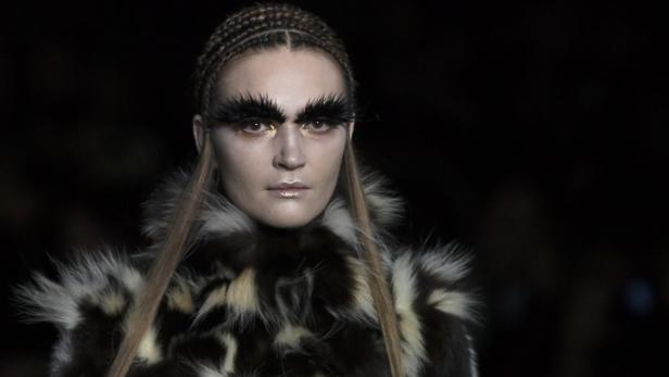 Eine Frau mit geflochtenen Zöpfen, Pelzkragen und übertriebenem Augenbrauen-Make-up.