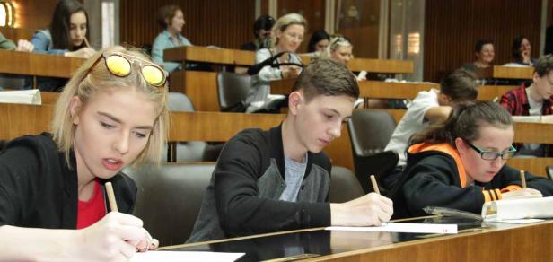 Schüler sitzen in einem Hörsaal und schreiben mit Stiften auf Papier.