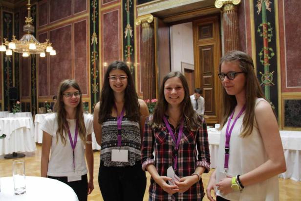 Vier junge Frauen stehen in einem eleganten Raum mit Namensschildern um den Hals.