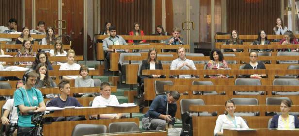 Viele Menschen sitzen in einem großen Raum mit hölzernen Bänken.