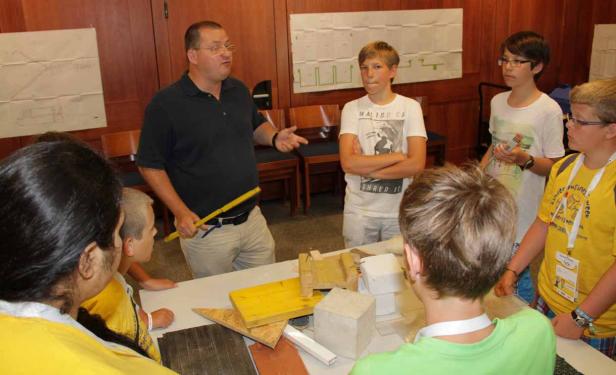 Ein Mann erklärt einer Gruppe von Kindern Baumaterialien und Baupläne.