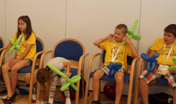 Vier Kinder sitzen auf Stühlen und spielen mit Ballonfiguren.