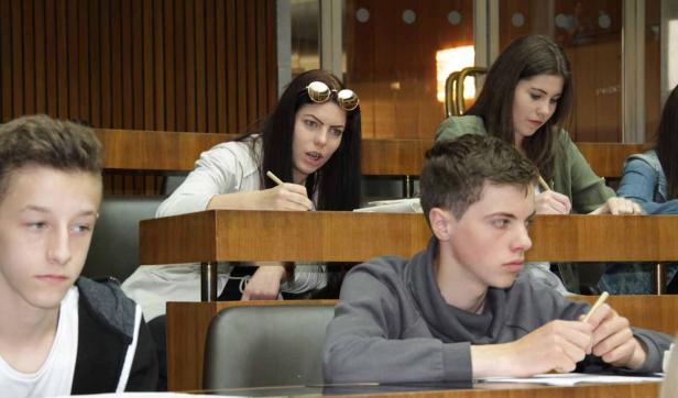 Mehrere Studenten sitzen in einem Hörsaal und schreiben mit Stiften.
