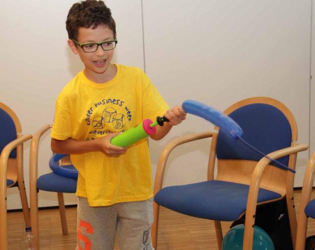 Ein Junge mit Brille pumpt einen blauen Ballon mit einer grünen Luftpumpe auf.