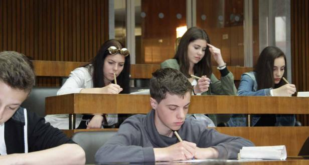 Mehrere Studenten sitzen in einem Hörsaal und schreiben mit Stiften.