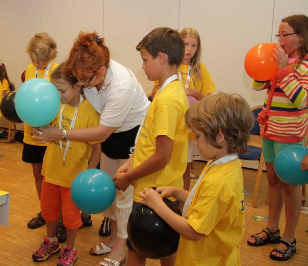 Eine Gruppe Kinder mit gelben T-Shirts und Luftballons, betreut von einer Frau.