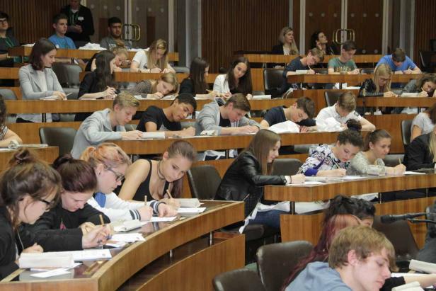 Viele Studenten sitzen in einem Hörsaal und schreiben Klausur.