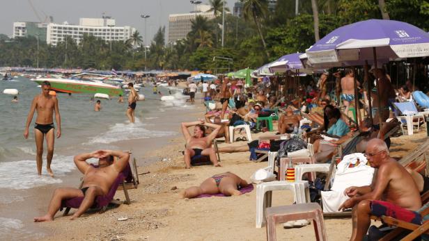 Ein belebter Strand mit vielen Menschen, Sonnenschirmen und Booten im Hintergrund.