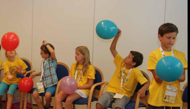Eine Gruppe Kinder sitzt auf Stühlen und spielt mit bunten Luftballons.