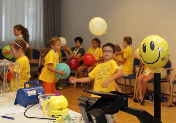 Eine Gruppe Kinder in gelben T-Shirts spielt mit Ballons in einem Raum.
