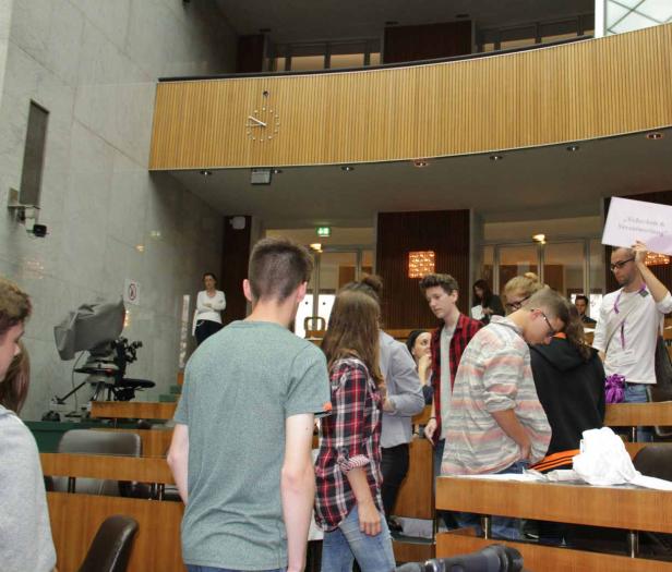 Eine Gruppe junger Leute steht im Zuschauerraum eines Parlamentsgebäudes, einer hält ein Schild mit der Aufschrift „Sicherheit & Verantwortung“ hoch.